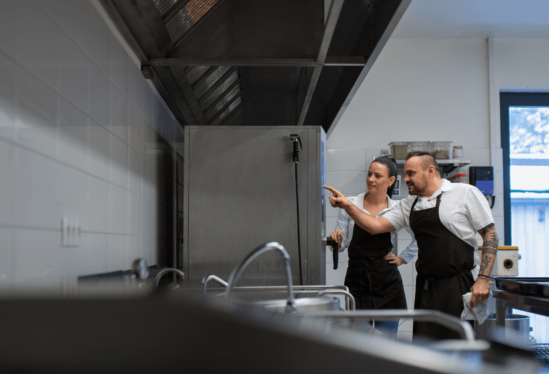 A chef is showing the sous-chef how to use the new combi oven the restaurant owner recently purchased. 